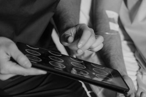 Grayscale Photo of a Doctor Holding a Digital Tablet